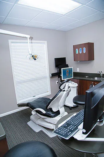 A treatment room with a dental chair and screens